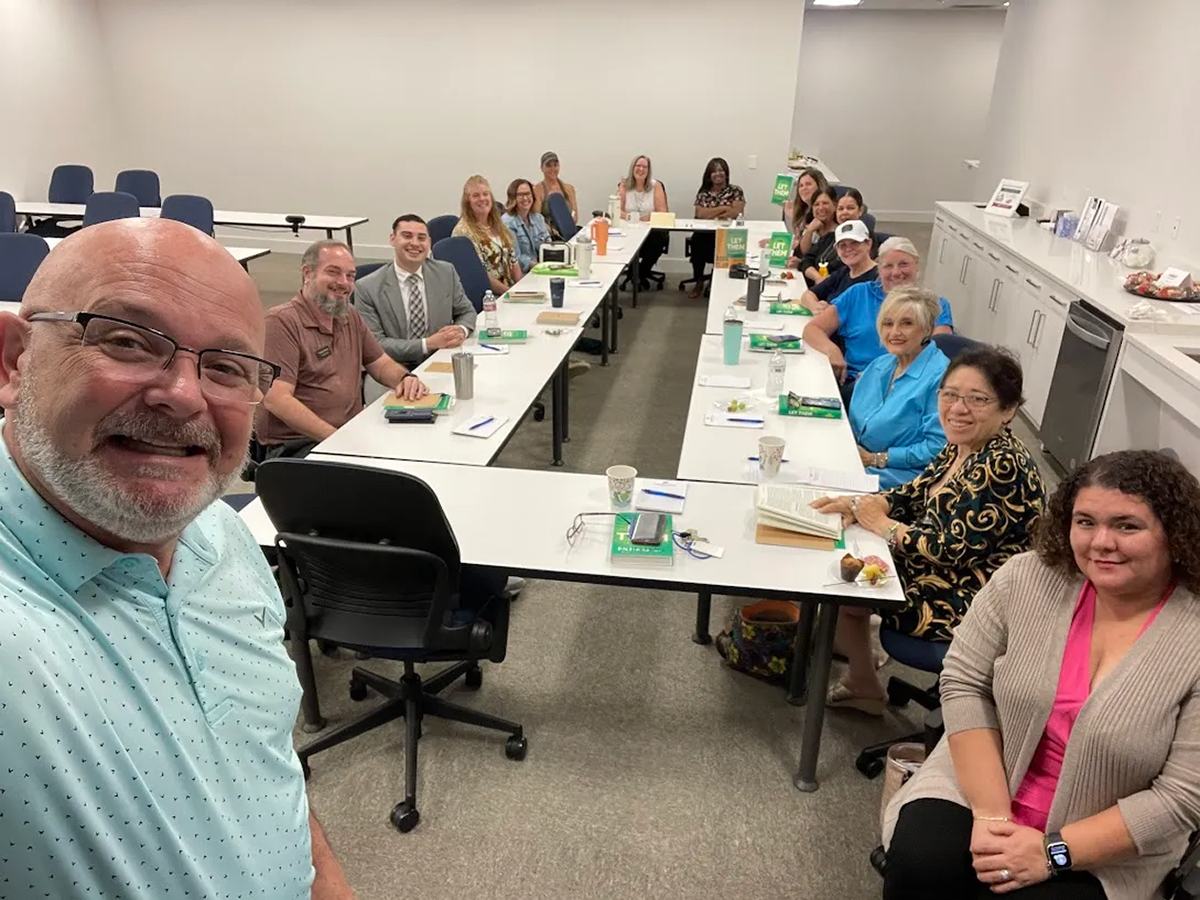Coach Matt Kern taking a selfie with his weekly business book club seated around long tables with books and coffee.